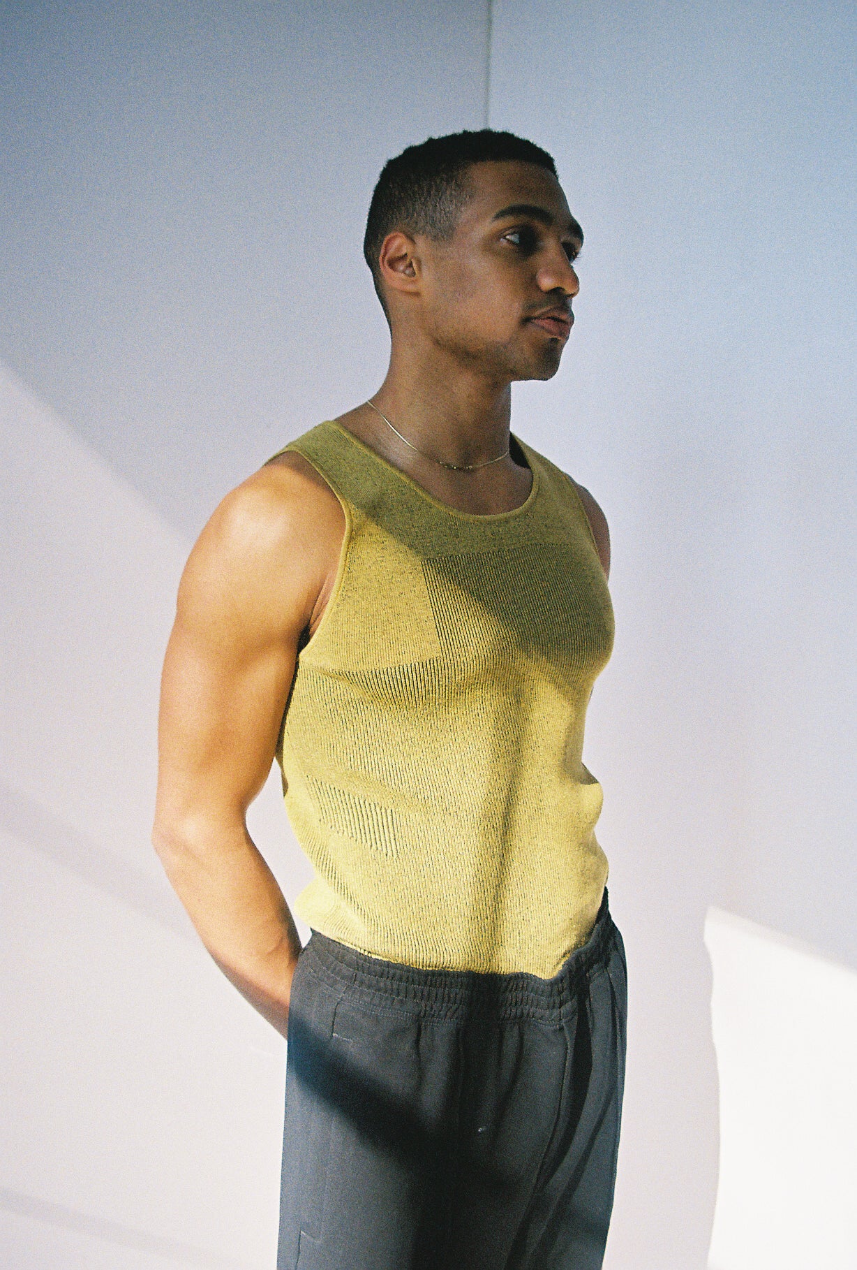 black man wearing yellow tank and black sweatpants staring into the distance thoughtfully