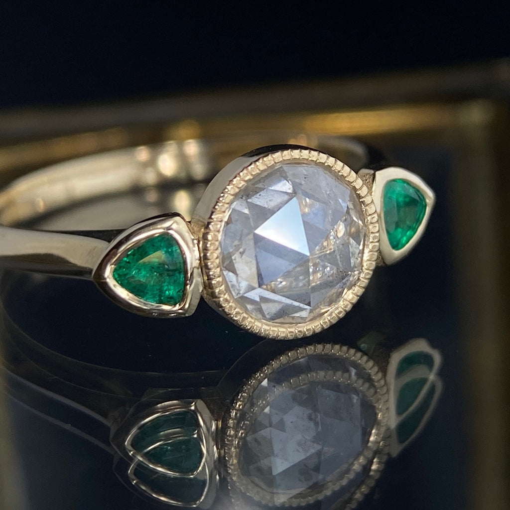 Miligrain is safely applied to bezel set diamonds, and a smoothe bezel encases vivid trillion emerald accents.