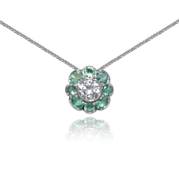 A floral inspired pendant showcases light color Brazilian emeralds around a white sapphire in platinum.
