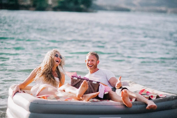 Image of a couple smiling while floating in a lake on a mattress.