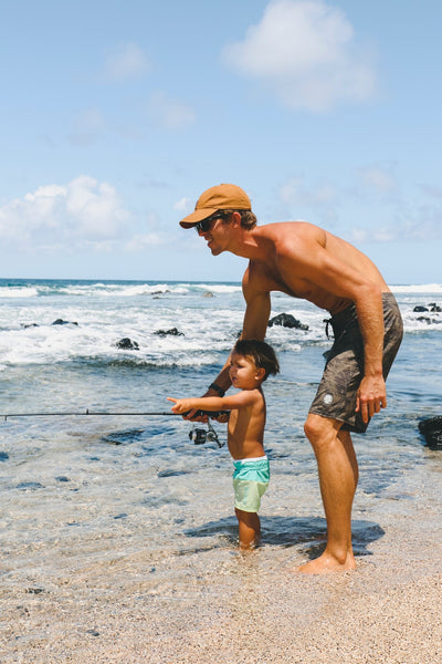10 Things to Do Before School Starts (For Families). Father playfully teaches toddler son how to use a fishing rod by the beach.
