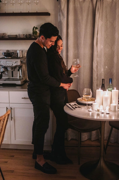 10 Ways on How To Be a Better Lover: Couple smiling and sharing an embrace next to their dinner date table at home.