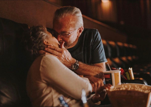 10 Ways on How To Be a Better Lover: Couple sharing a kiss as they sit at a movie theater.