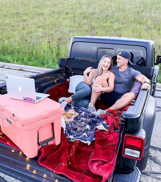 A couple cuddles in the bed of truck while watching a movie on a laptop.