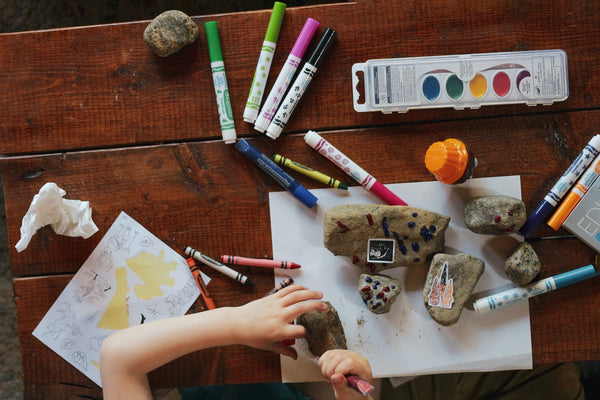 Little girl collecting rocks and painting it with her coloring materials sprawled on her desk
