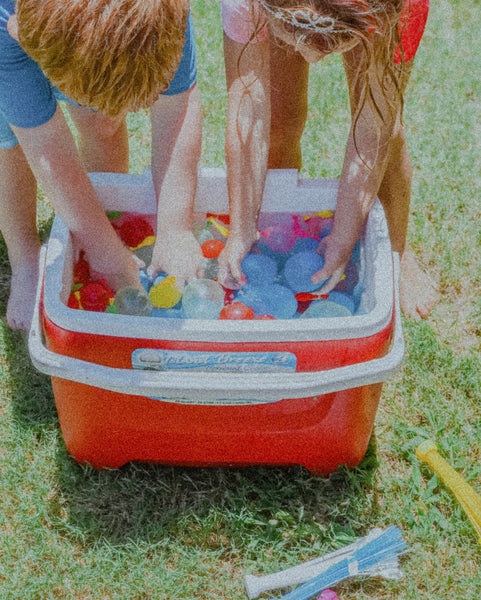 Two kids grabbing water balloons from a cooler in their garden