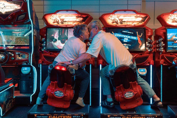5 date ideas to celebrate national couple’s day: Elderly couple sharing a kiss as they sit on motorcycles at the arcade.