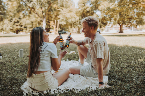 5 date ideas to celebrate national couple’s day: Couple sharing a toast with their beer during their picnic date.