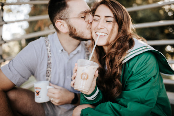 5 date ideas to celebrate national couple’s day: Guy planting kiss on his girlfriend's cheek as they share coffee together.