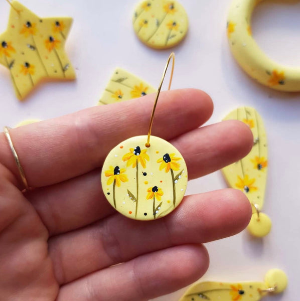 Person holding up yellow hand-painted clay earrings