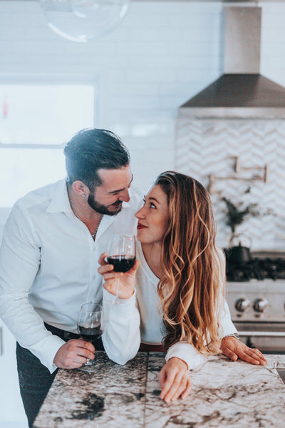 55 Cheap Date Ideas That Are Fun And Create Connection. Couple smiling at each other in the kitchen with woman holding glass of wine.