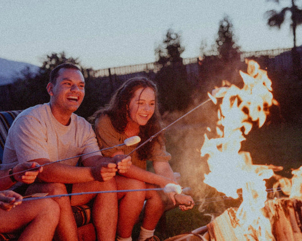 55 Cheap Date Ideas That Are Fun And Create Connection. Couple smiling as they sit around a bonfire and make smores.