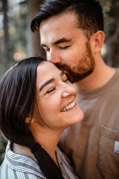 Image of a woman smiling as her boyfriend kisses her on the forehead.