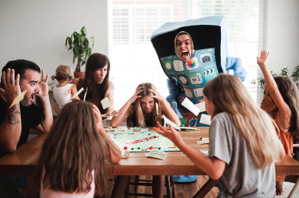 A family looks distraught as they sit at a table and a guy in an iPhone costume yells at them