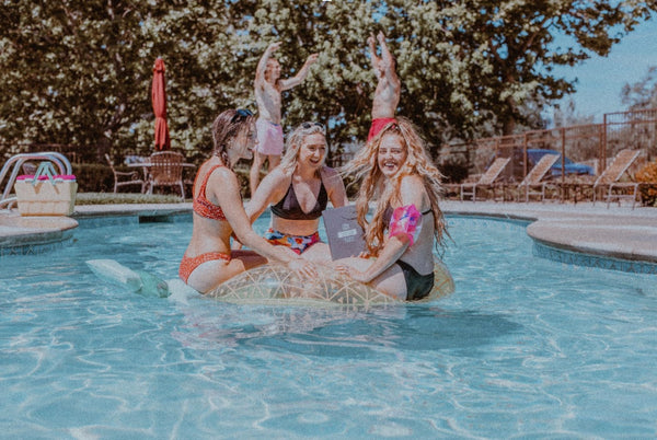 A group of girls float on a pool floatie together in a swimming pool