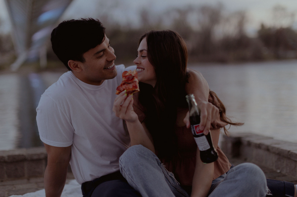 Conversation Starters for Married Couples: Wife smiles as she holds her pizza as her husband wraps his arm around her while holding a bottle of coke