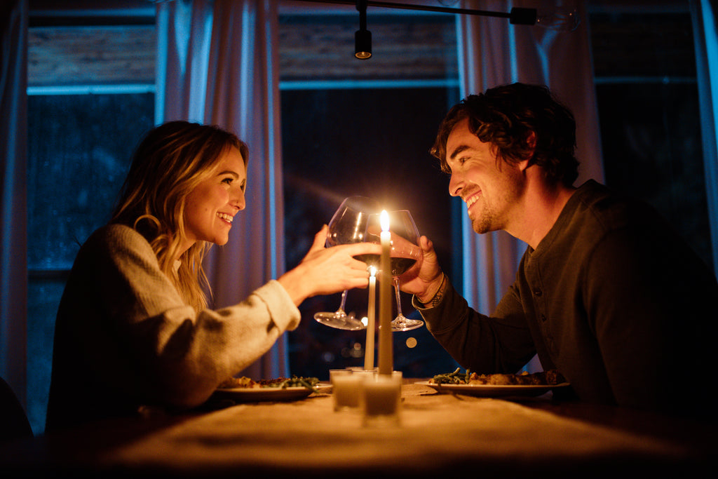 Couple smiling at each other and sharing a toast during their romantic candlelit dinner