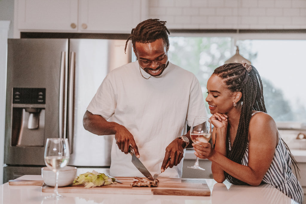 Reignite the spark in your relationship with weekly date nights. Couple smiling as they lean against kitchen counter while preparing for date night.