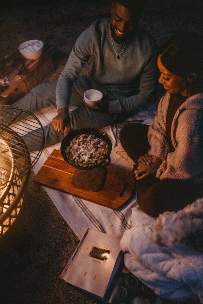 Couple smiling as they cook together during their outdoor date at night