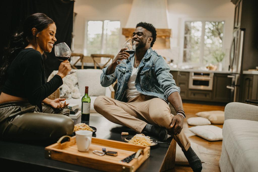 Couple laughing together as they sip on their wine during their date in the living room