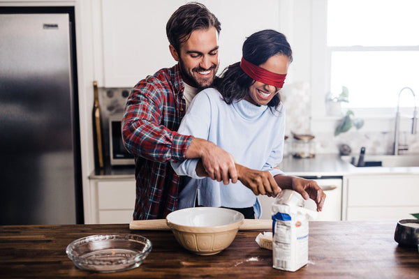 Adventure Ideas Just About Anyone Can Do: Couple tries blindfold baking with the guy guiding the blindfolded girl with measuring the flour