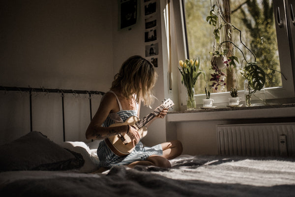 Girl picking up a new skill and learning the guitar as she sits on her bed next to her window