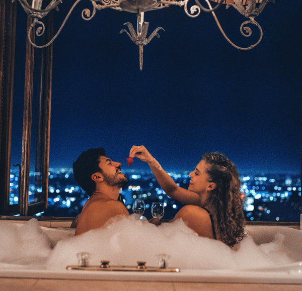 At Home Date Night Ideas: Couple feeding each other strawberries in a jacuzzi with a view of the city