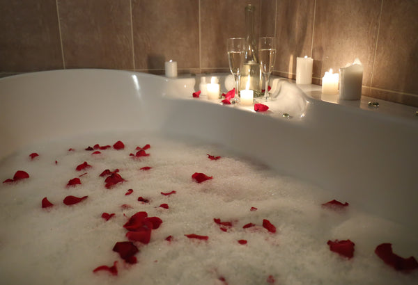 Bedroom Decoration Ideas to Make Your Anniversary More Romantic. Rose petals placed on a bubble bath with candles at the side.