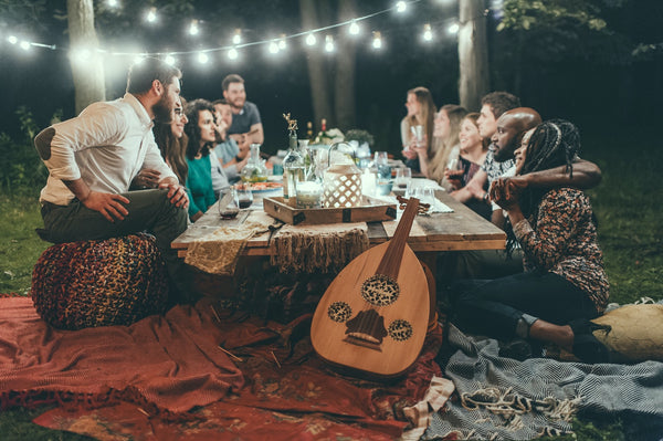 A group of friends sat around a table having a lighthearted discussion with a guitar resting against the table and string lights behind them