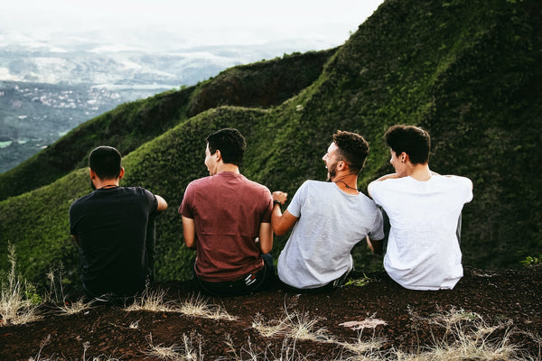 Four guy friends sharing laughs while sitting on a ledge in front of a lush mountain view