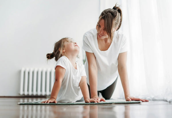 Mother and daughter smiling at each other as they do some yoga poses 