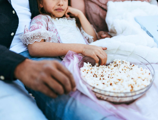 Sleep-Promoting Bedtime Snack: Close-up shot of little girl leaning against his father's chest as they both enjoy a bowl of popcorn.