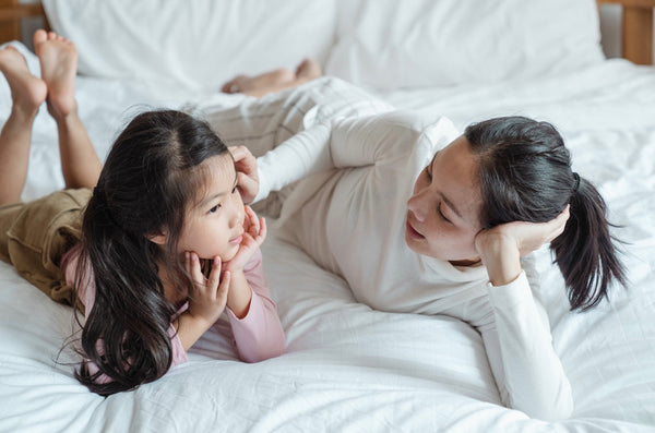 Chat or Talk to Them About Their Day: Mother talking to her daughter as they both lie in bed.