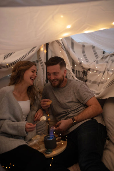  Cheap Date Ideas (That Don't Feel Cheap). Couple share laughs as they roast marshmallows in the fort that they built and decorated with fairy lights.