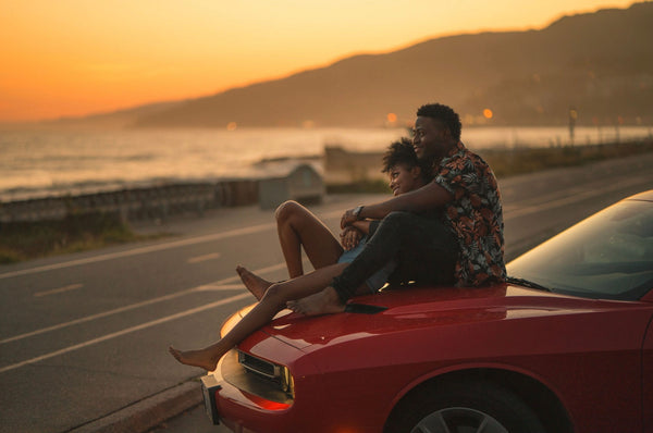  Cheap Date Ideas (That Don't Feel Cheap). Couple smile as they watch the sunrise on the hood of their car.