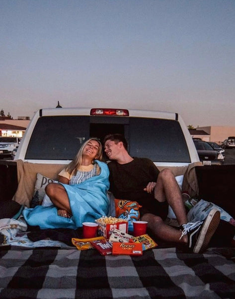  Cheap Date Ideas (That Don't Feel Cheap). Couple snuggle at the back of their pick-up truck with some snacks as they enjoy a drive-in movie.