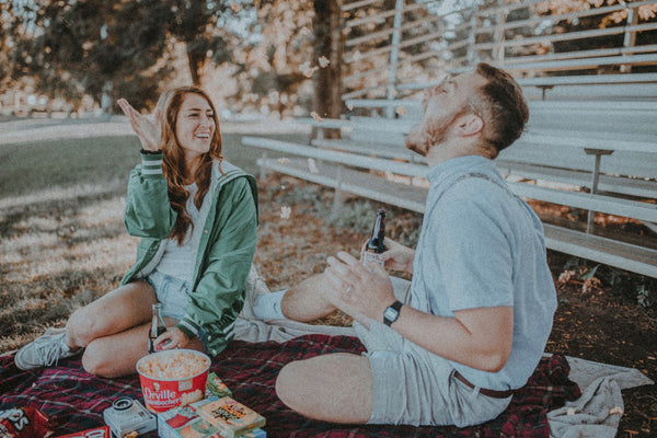  Cheap Date Ideas (That Don't Feel Cheap). Couple having an outdoor picnic together, with the girl feeding the guy popcorn.