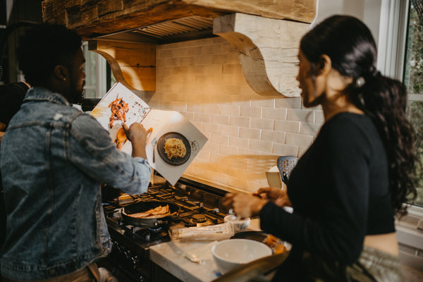 Creative, Romantic, and Fun Stay-at-Home Date Ideas for Couples: Couple making dinner together with a cookbook