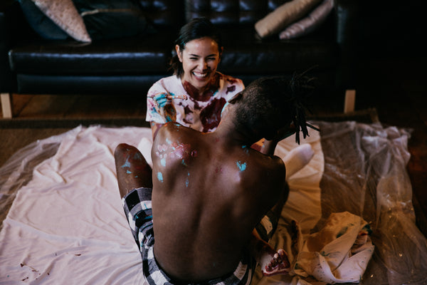 How The In Bed Book Helps Create Sexual Passion and Intimacy. Couple smiling as they squat on the floor with paint on them.