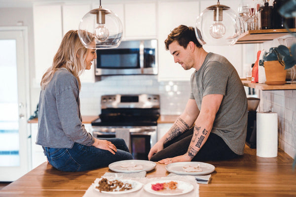 A couple sit on a counter together next to plates of food as they discuss conflict together