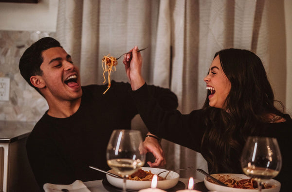 A woman feeds her boyfriend spaghetti as they smile together
