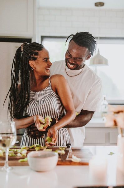 How to Increase Intimacy in a Relationship. Guy hugs girl from behind and smiles as she smiles back while she works on a meal on the kitchen counter. 