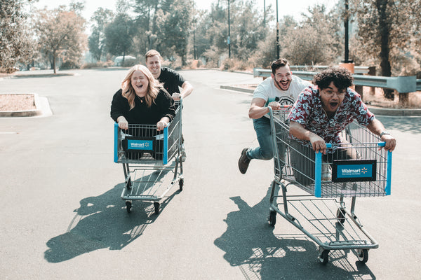 Image of two friends pushing shopping carts that their friends are riding in as a way to have fun and invest in friendships together.