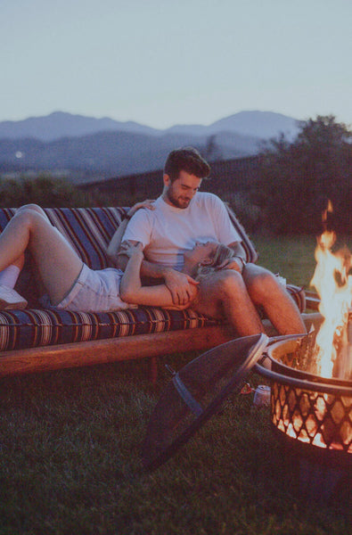 The Adventure Challenge: Couple lounging outside by the fire as they talk to each other.