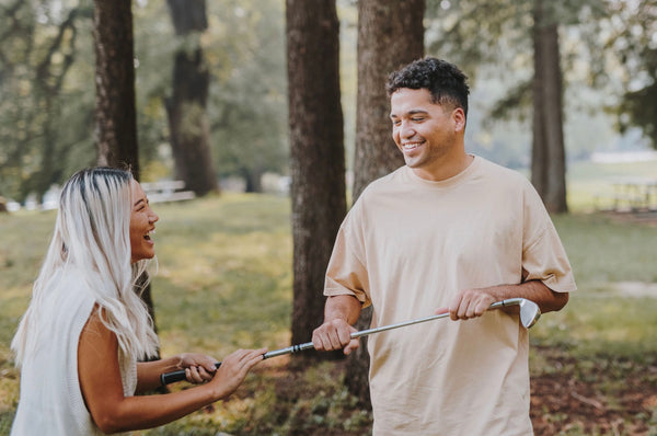 93 Best Conversation Starters for Couples to Better Connect: Couple on a date outdoors laughing while holding a golf club.