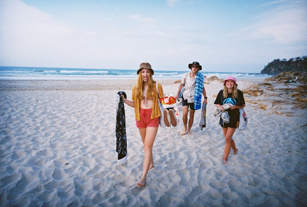 Three teenage kids strolling along the sand by the beach carrying their shoes and extra clothes