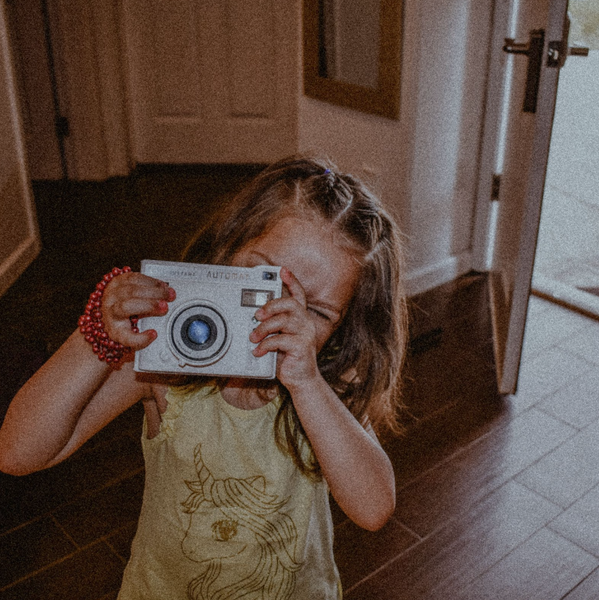 Little girl holding up a polaroid camera and looking into the lens as she is about to take a photo