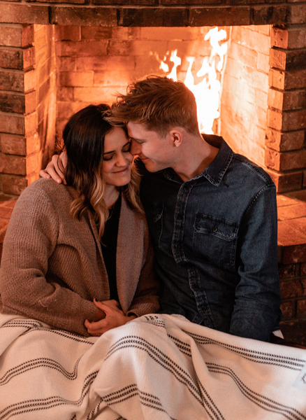 Couple in a warm embrace with a blanket draped over their legs as they sit by the fire