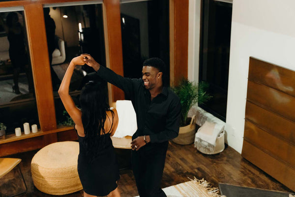 Couple dancing with each other in their living room as the guy smiles as they celebrate their anniversary