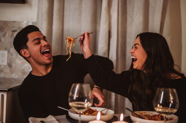 Couple sharing laughs as they feed each other spaghetti during their anniversary dinner date